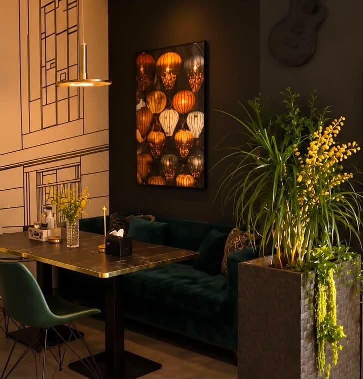 Colț cu banchetă verde, plante și lămpi calde în restaurantul Capitale